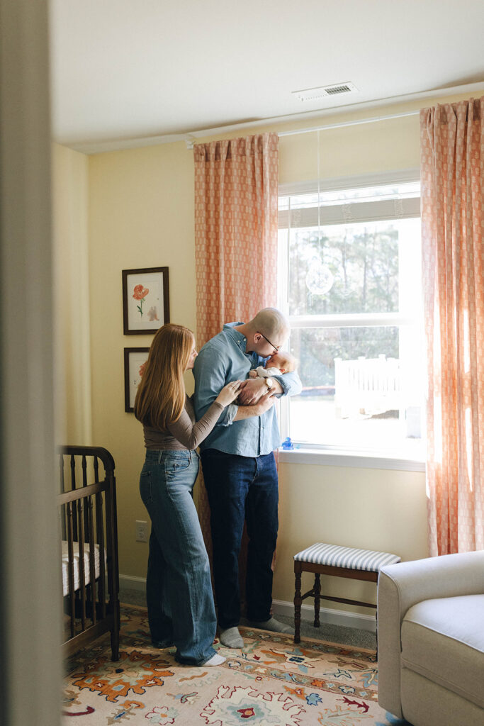 Candid photo of mom and dad kissing their newborn baby in the nursery