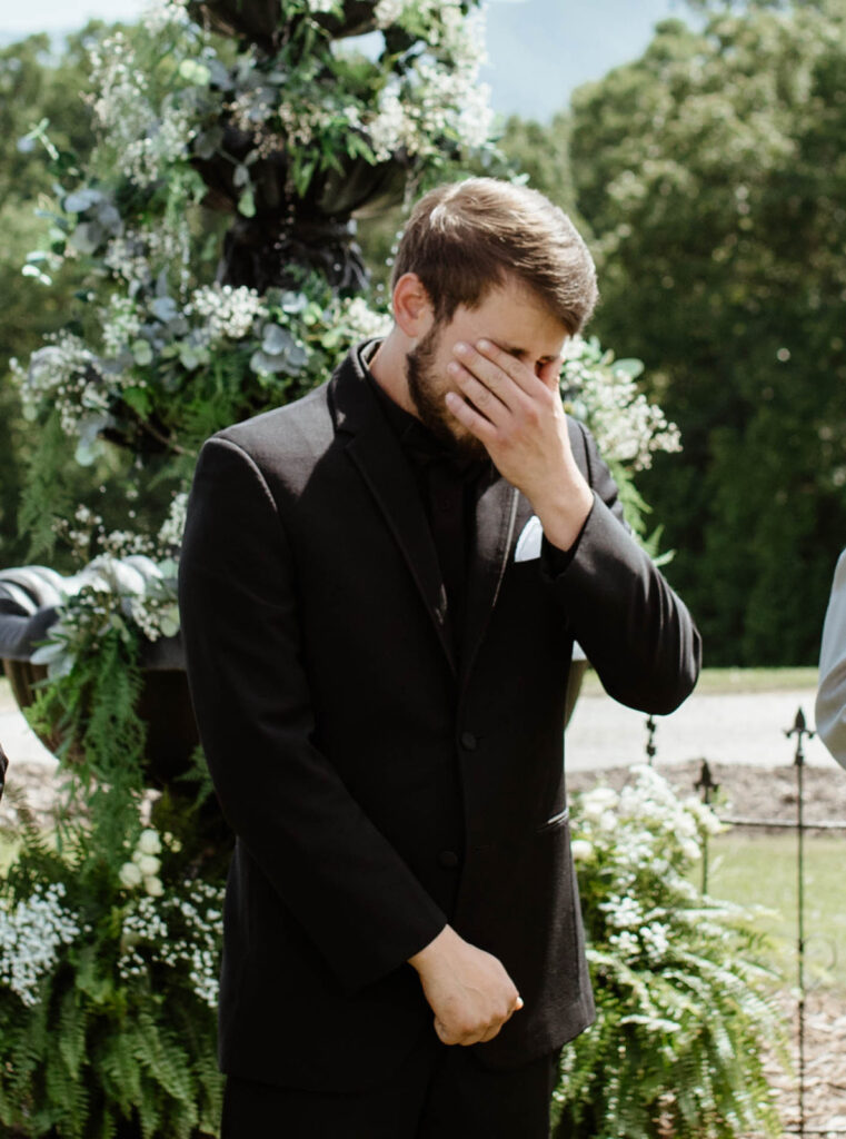 Groom wiping away tears while watching bride walk down the aisle at a North Carolina wedding