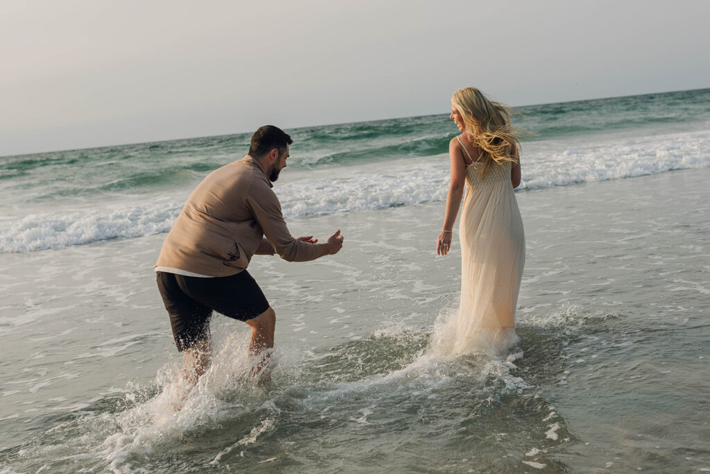 Couple splashing each other in ocean during sunrise beach couples session in Wrightsville Beach