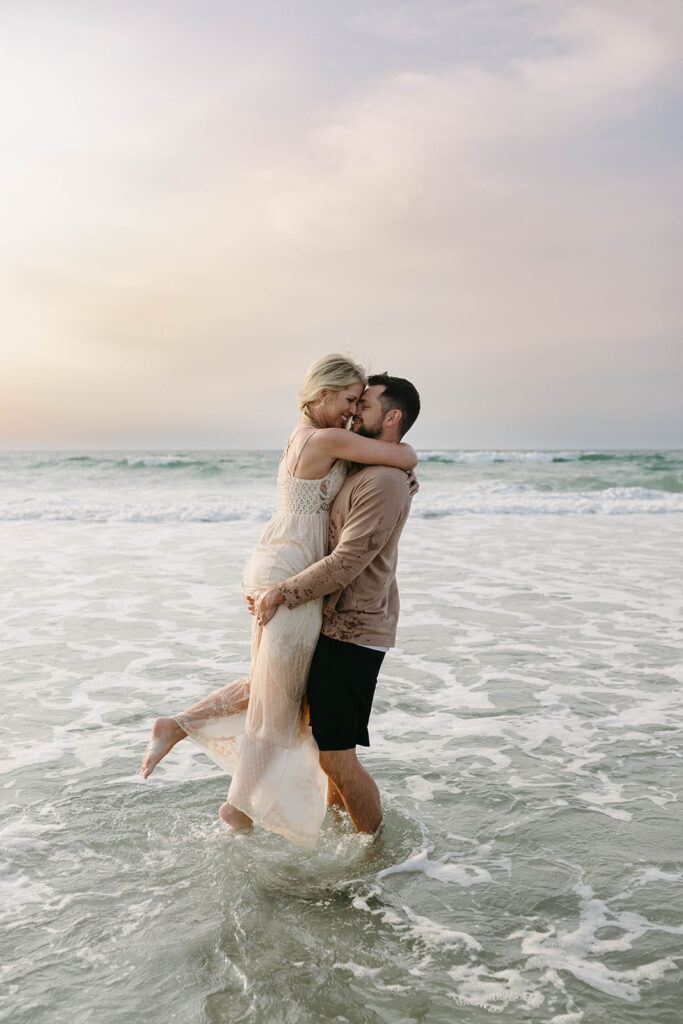 Couple embracing at sunrise on Wrightsville Beach with soft pastel sky