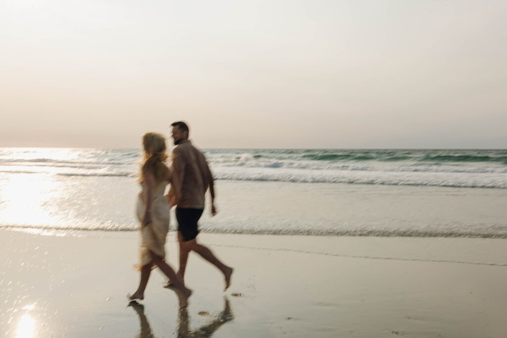 Vacationing couple running hand-in-hand during a beach photo session in Wrightsville Beach