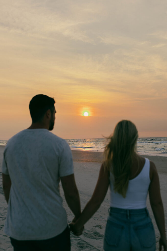 Vacationing couple walking hand-in-hand during a sunrise beach photo session in Wrightsville Beach
