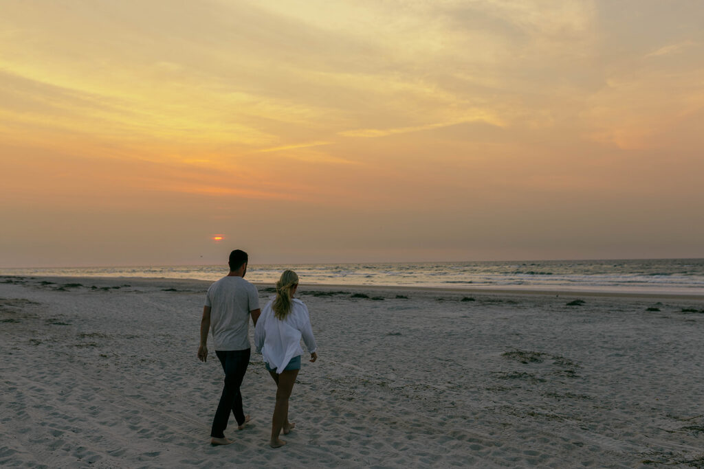 Vacationing couple walking hand-in-hand during a beach photo session in Wrightsville Beach